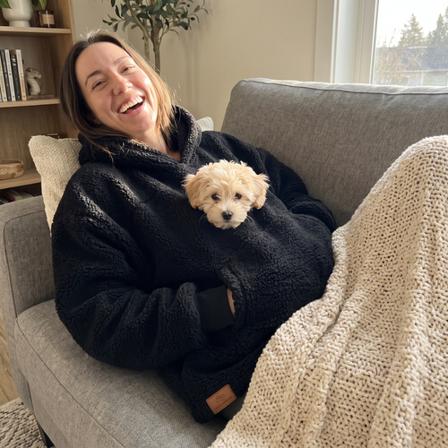 Black Pawket hoodie with a small puppy in the pocket on the couch
